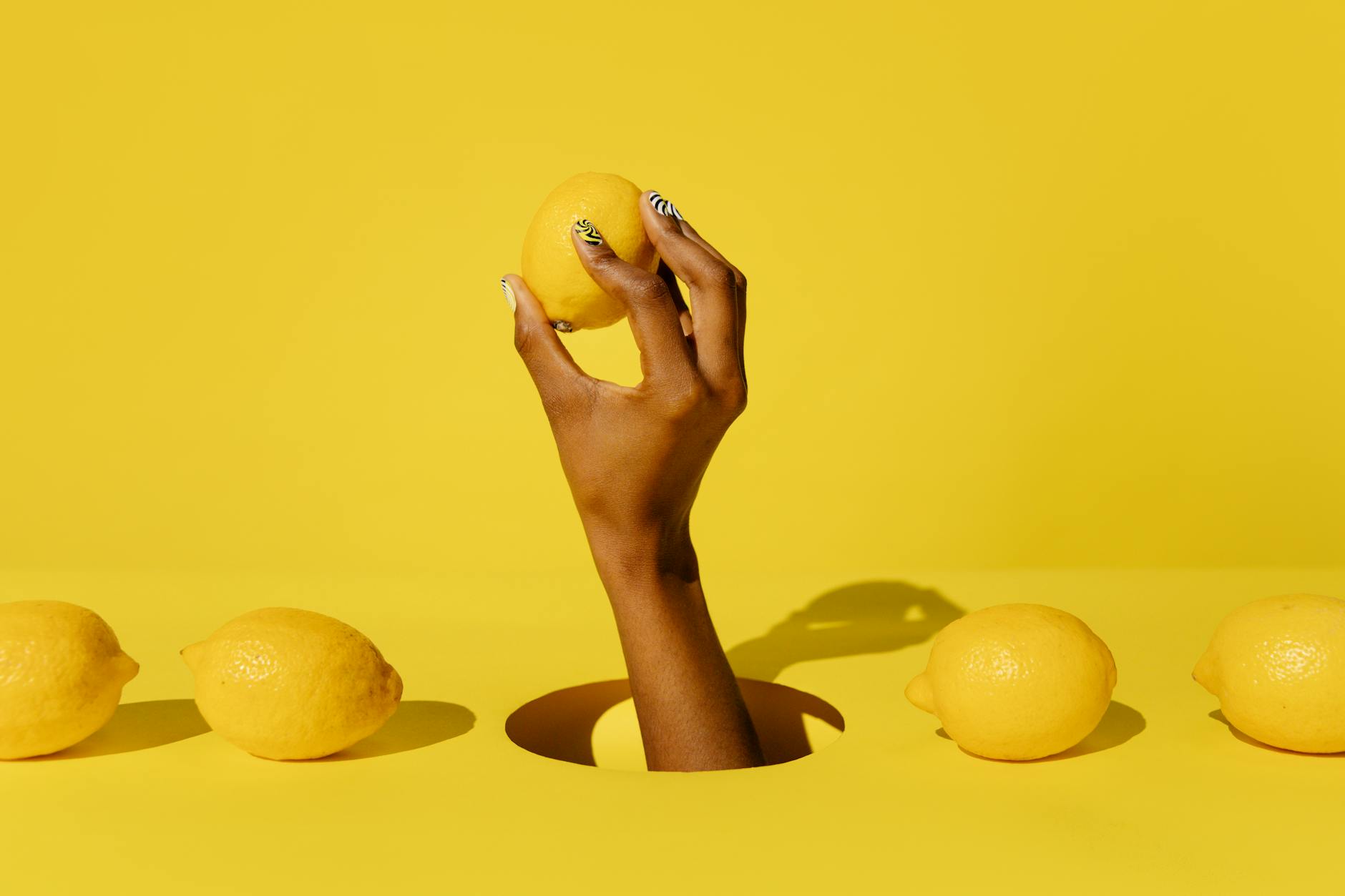 A hand holding a fresh lemon against a vivid yellow background, symbolizing the bright, modern design of lemon vibrators