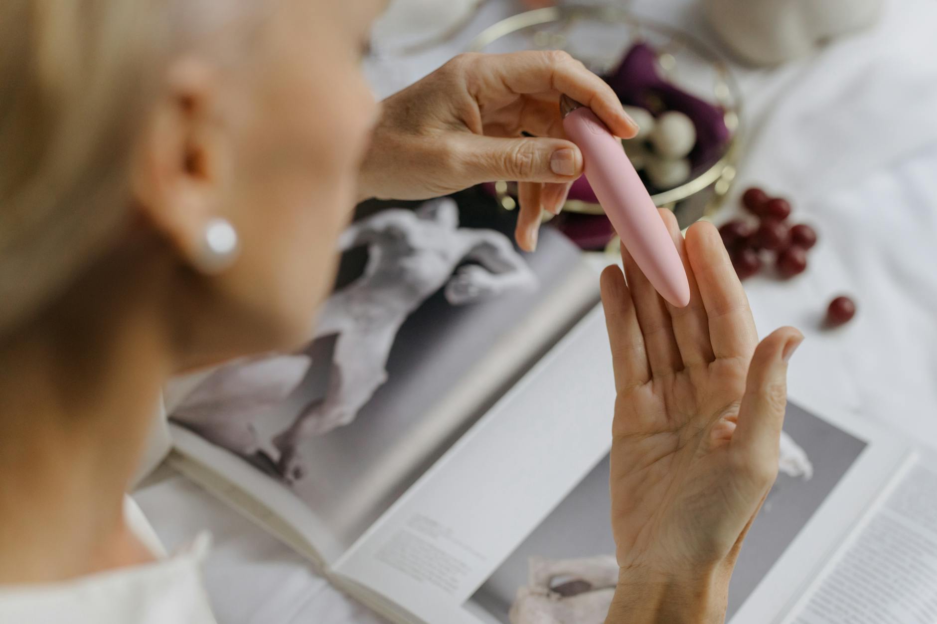 Close-up of a woman holding a pink vibrator, with art books in the background