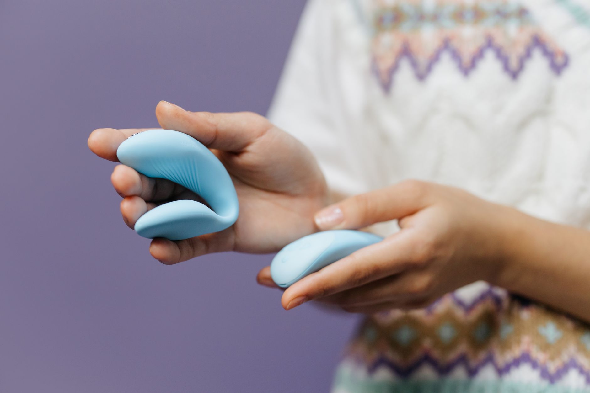 Close-up of hands holding a sleek blue vibrator against a purple background, representing modern intimate pleasure.