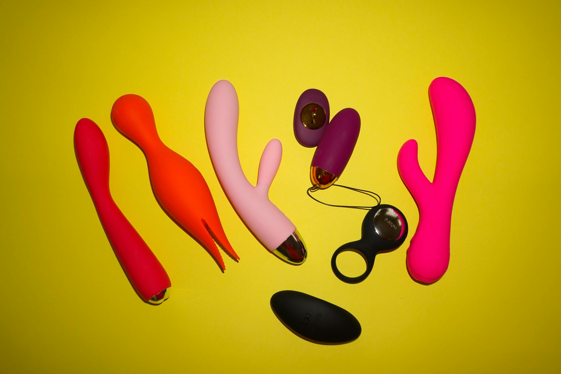 Colorful sex toys arranged on a bright yellow background, including clitoral vibrators and adult toys